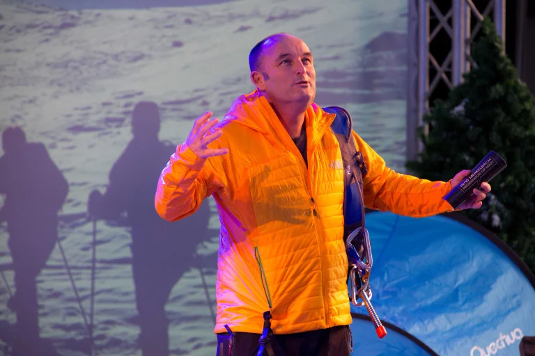 Rens Merkelbach in een oranje jas, die een presentatie geeft tijdens een evenement.